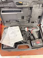 Open hard case with drill, two batteries, charger, manuals