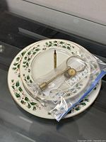 Two porcelain plates with holiday holly pattern and bagged brass hardware on glass surface