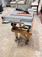 Ridgid table saw side view on wooden stand, rip fence attached, blade guard visible