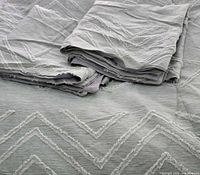 Folded grey tufted comforter and shams with geometric embroidery
