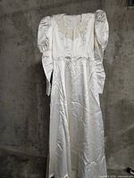 Full view of satin wedding dress hanging, showing train and sleeve shape
