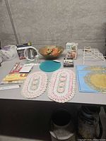 Table layout showing all items including bowl with faux fruit, silicone mat, boxed items, toiletries, rack, and crochet doilies