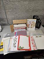 Overview of lot showing boxed invitation kit, assorted decorative papers, folders, envelopes and plastic sleeves