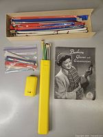 Box of assorted knitting needles, zip bag with packaged needles/hooks, yellow storage tube with needles, small yellow accessory, Beehive pattern booklet