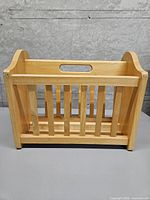 Front view of oak-coloured wooden magazine rack with slatted sides and handle