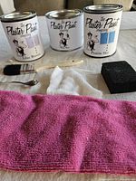 Overview of three Plaster Paint Company cans, brush, cloths, spoon, sanding block