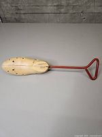 Full view of shoe stretcher showing wooden body and red metal handle