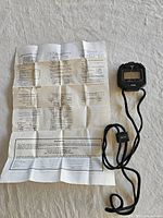 Stopwatch with lanyard alongside instruction sheet fully unfolded