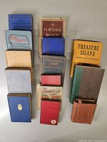 Group shot of thirteen hardcover books arranged in three columns, showing spines and covers