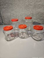 Five identical clear glass jars with red lids