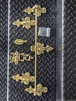 All brass components laid out: towel bar, three fleur-de-lis plates, hook, ornate plate, screws