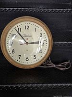 Full view of round Telechron wall clock showing wood frame, dial and cord