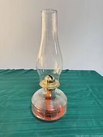 Front view of clear glass oil lamp showing reservoir, brass burner and chimney