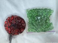Mesh bag of red gems next to zipper bag of green gems on white background