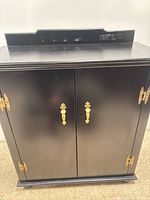 Front view of black wood cabinet showing two doors with brass-tone pulls and hinges