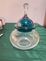 Clear spherical glass jar with blue-teal lid and clear finial displayed on table