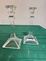 Two clear glass geometric Art Deco candlesticks on green surface