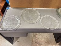 Three clear pressed glass serving platters on tabletop showing size and floral pattern