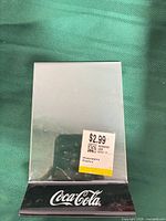 Front view of single menu holder showing clear panel, black base, Coca-Cola logo