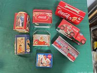 Group shot of eight Coca-Cola metal tins displaying shapes and themes
