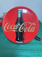 Front view of round red Coca-Cola wall telephone showing bottle graphic and script