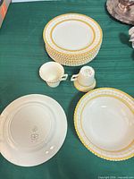 Stack of yellow-border dinner plates, one soup bowl, two cups, showing pattern