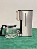 Side profile of coffee maker with glass carafe showing stainless steel finish and water level indicator