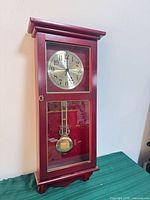 Front view of wall clock showing dial, pendulum, wood and glass case