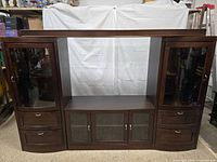 front view showing entire entertainment center with side cabinets, central opening, drawers and glass doors
