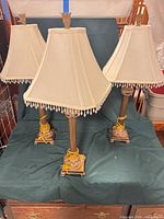 Three metal table lamps with shades displayed on surface