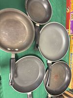 Top view of five pans displaying interiors, handle style and wear