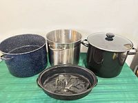 Four large cookware pieces: blue speckled stock pot, stainless stock pot, black enamel stock pot with glass lid, black enamel oval roasting pan