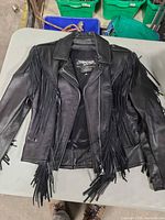 Front view of black leather fringe jacket laying flat on table