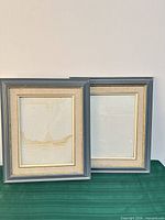 Front view of both gray-blue wood frames with gold trim, glass and mats