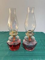 Front view of both glass and brass kerosene lamps with chimneys, burners, red fuel visible