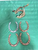 Group of horseshoes laid out on green surface showing four singles and one welded decorative piece