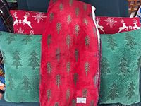 Blanket folded over green tree patterned pillows with red reindeer patterned pillow behind