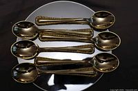 six gold-plated spoons laid out bowl-up on reflective surface