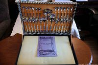 Open case displaying all flatware pieces strapped to lid with booklet and foam insert below