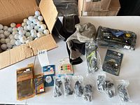 Open box of golf balls, headcovers, cleats and accessory packs on table