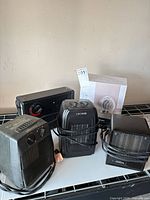 Group of five heaters visible including boxed Mainstays unit and four used black heaters