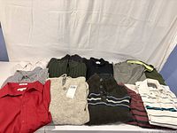 Overview of eleven shirts and sweaters laid out on table