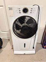 Full front view of white pedestal misting fan showing grille, water window, cord