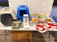 Overall lot view showing carrier, litter box, feeders, bowls, toys, outfits