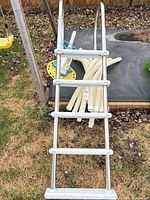 Ladder leaning against raised surface with pool cleaner head and hoses visible