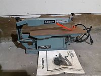 Full view of Delta 15-inch scroll saw with manual and accessories on floor