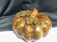 Full view of glazed ceramic pumpkin showing ribbed body, stem and leaves