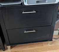 front view of black two-drawer filing cabinet with metal handles and legs