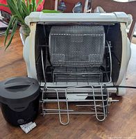 George Foreman rotisserie opened showing wire basket, spit attachment and Proctor Silex warming pot in front