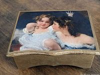 Closed gold-tone wooden jewelry box with printed artwork lid